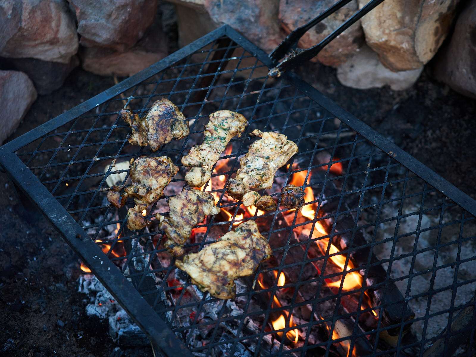 grilling chicken over the campfire on a grill grate 