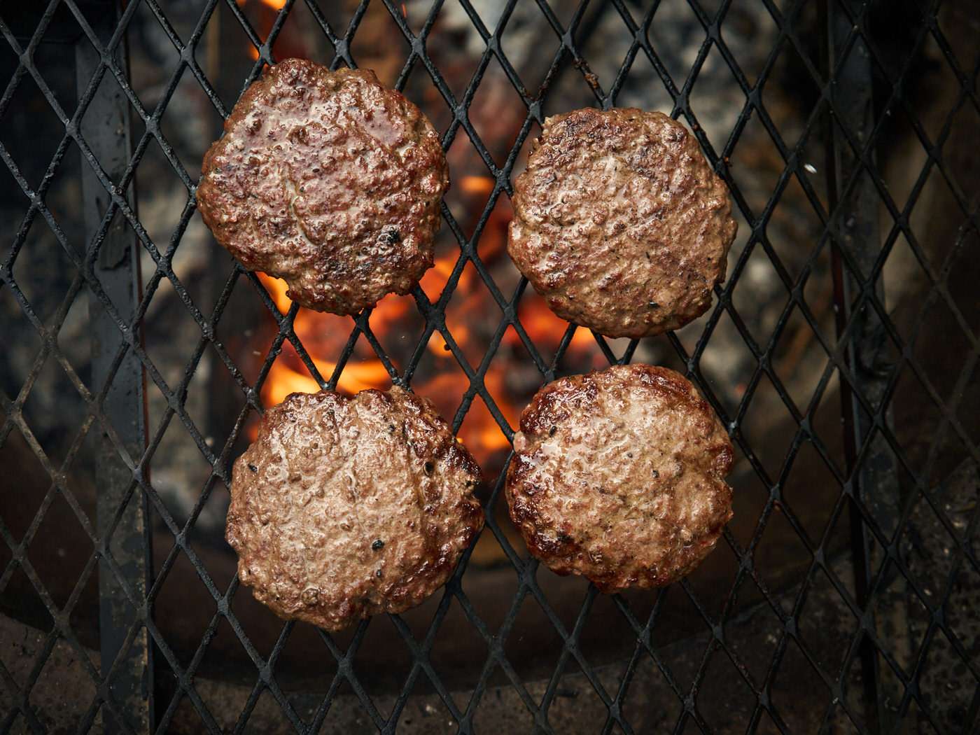 grilling beef burgers over the campfire on a grill grate