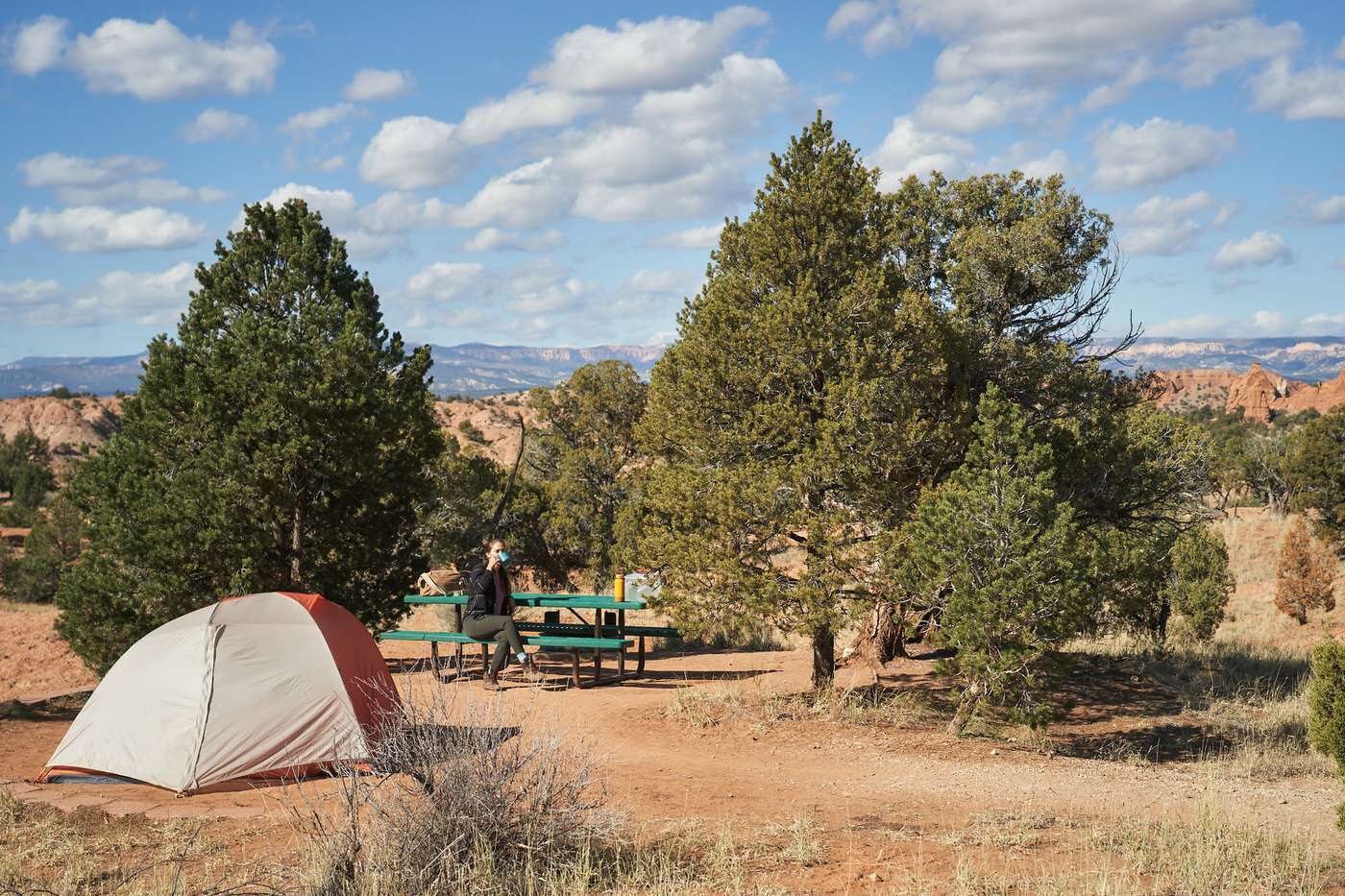 campsite in Kodachrome State Park with a tent, green picnic table, and Amanda sipping coffee