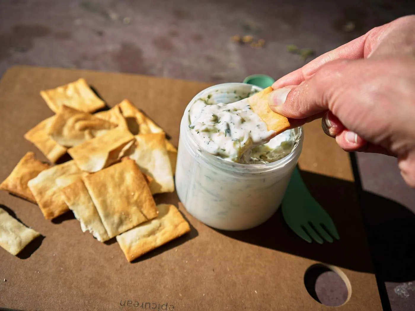 scooping tzatziki on a pita chip for a quick camping snack