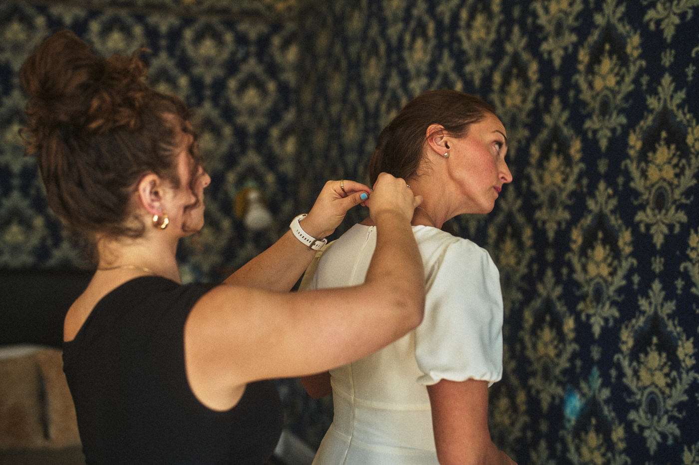 bride getting ready for her wedding with the help of a friend 
