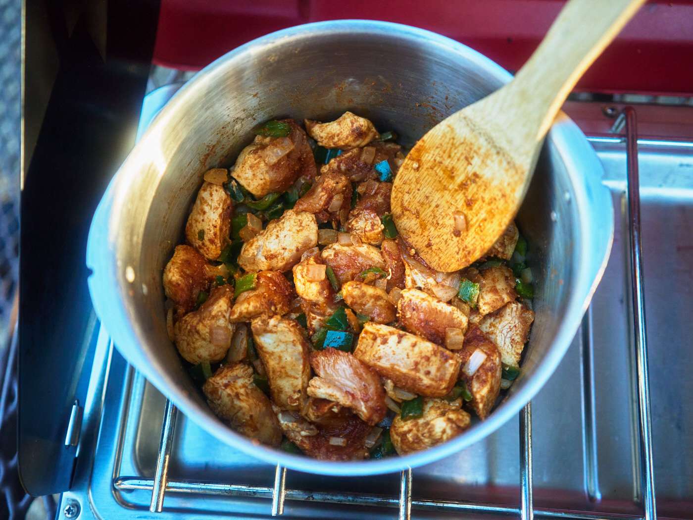 camp stove cooking chicken with spices, peppers, and onions 