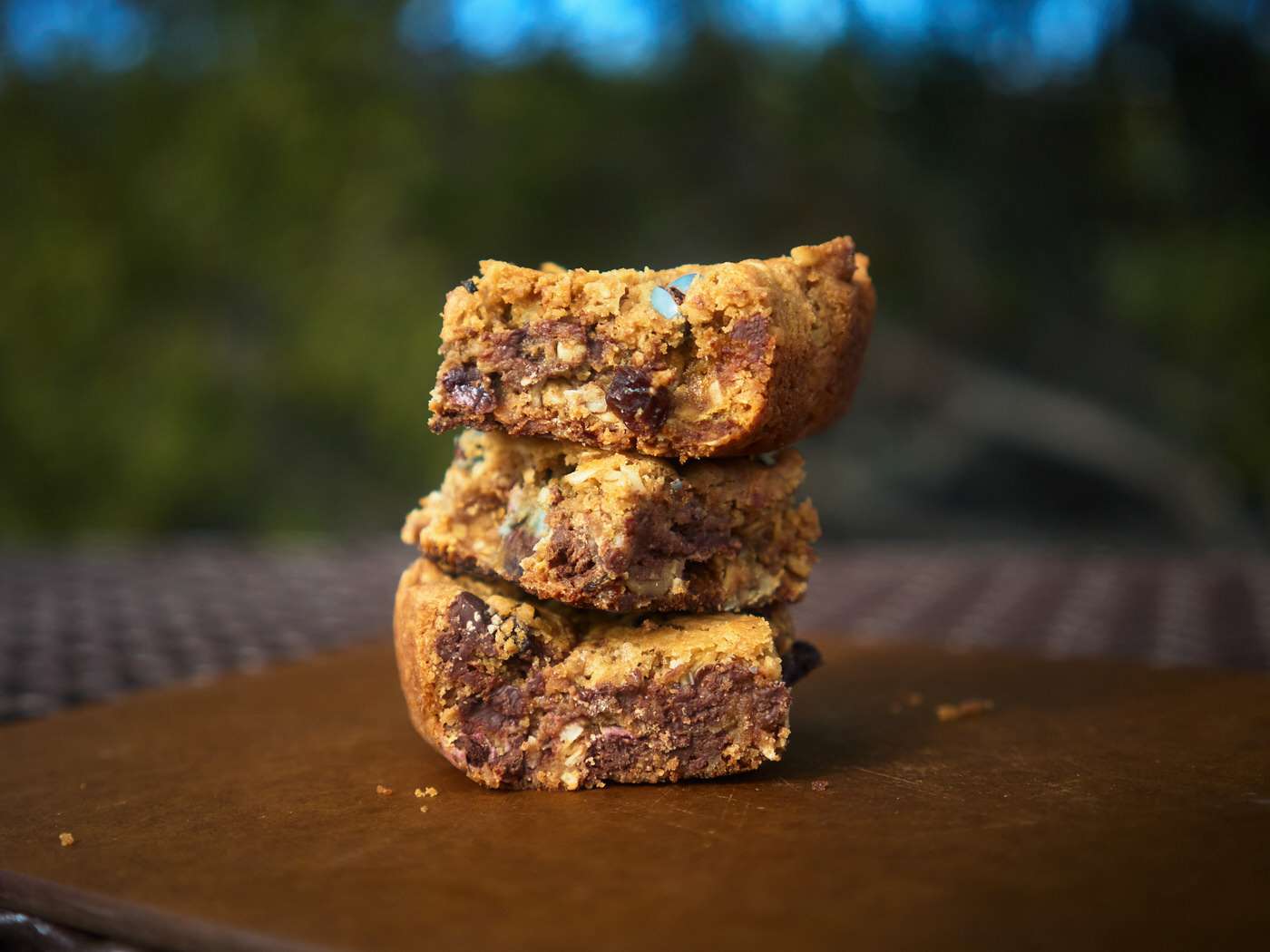 stack of three trail mix cookie bars on a picnic table outside 