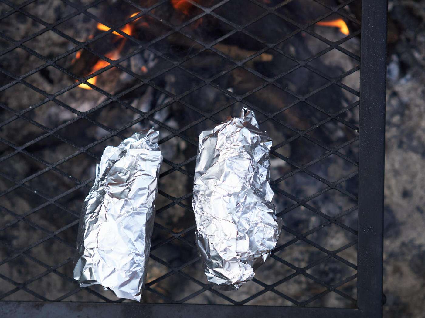 Foil-wrapped campfire cones cooking over a campfire grate