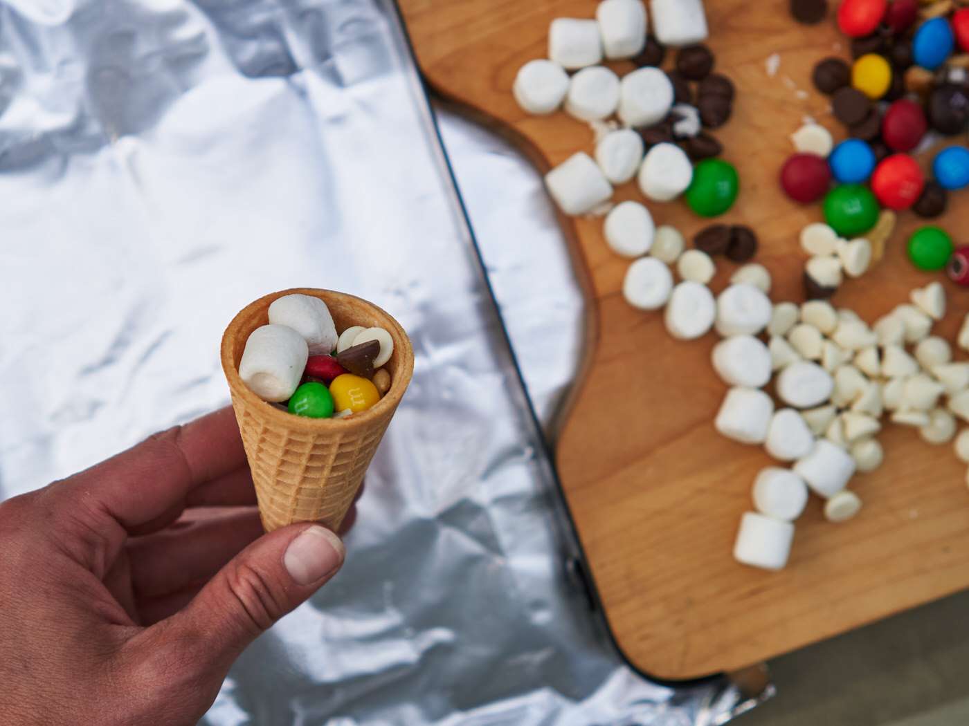 Filling waffle cones with marshmallows, chocolate, and nuts to make campfire cones