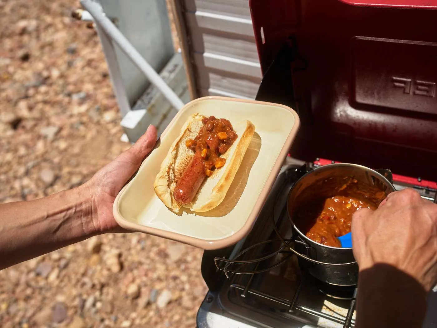 topping a beef hot dog with chili while camping